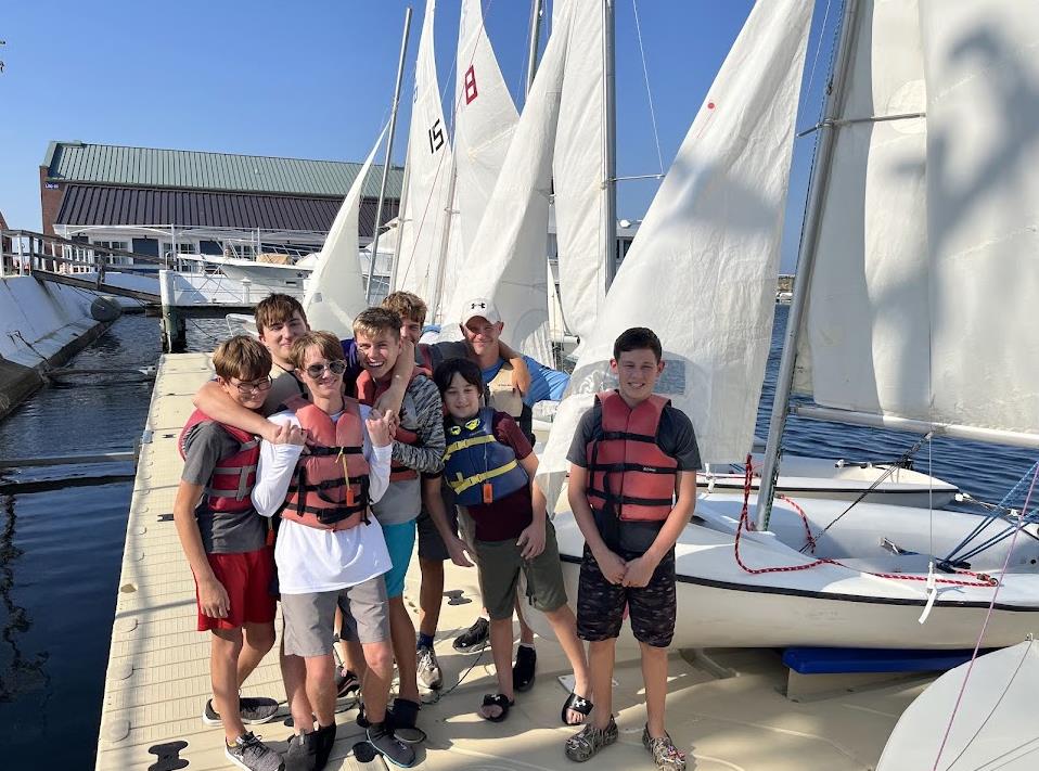 group of kids smiling next to a bunch of sailing boats